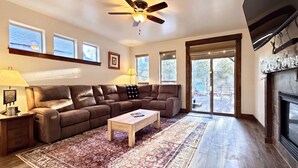 A living room with a brown leather sectional sofa, a wooden coffee table, a patterned rug, a ceiling fan, and a fireplace. - The Timberline Haus - Where Pines Meet The Payette (McCall)