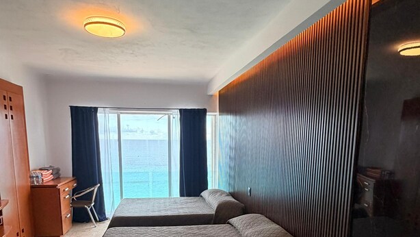 Ein Hotelzimmer mit zwei Betten, einer großen Badewanne, einem Holzschrank, einem Schreibtisch und Meerblick.