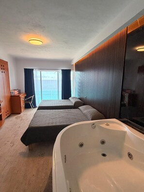 Een hotelkamer met twee bedden, een groot bad, een houten garderobe, een bureau en uitzicht op zee.