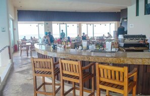 A bar area with a counter, stools, and a view of the sea. - LUNA Y SOL CARIBE SUITES BY CANCUN PLAZA (Cancún)