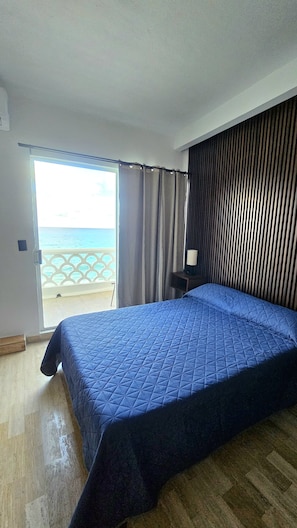 A room with a bed, a nightstand, a lamp, a view of the sea, and a sliding door. - LUNA Y SOL CARIBE SUITES BY CANCUN PLAZA (Cancún)
