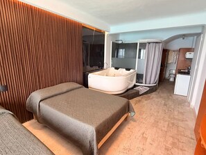 Een slaapkamer met een groot bed, een badkuip, een douche en een kleine kitchenette.