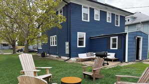 A blue house with a patio area featuring wooden Adirondack chairs, a round wooden table, and a barbecue grill. - Superlisting! Entire Duplex, perfect for 2 families traveling together (Sioux Falls)