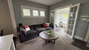 A living room with a dark-colored sofa, a round coffee table with a plant, and a large window with a view of the outdoors. - Superlisting! Entire Duplex, perfect for 2 families traveling together (Sioux Falls)