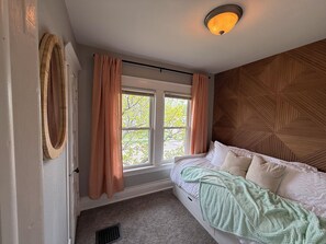 Un dormitorio con cama, una ventana con cortinas, una lámpara de pared y una pared con textura de madera.