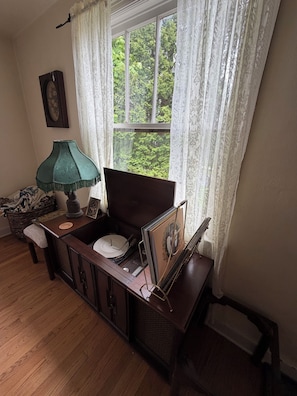A room with a wooden cabinet, a lamp, a window with curtains, and a framed picture on the wall. - Charming 3-bedroom house in State College (State College)