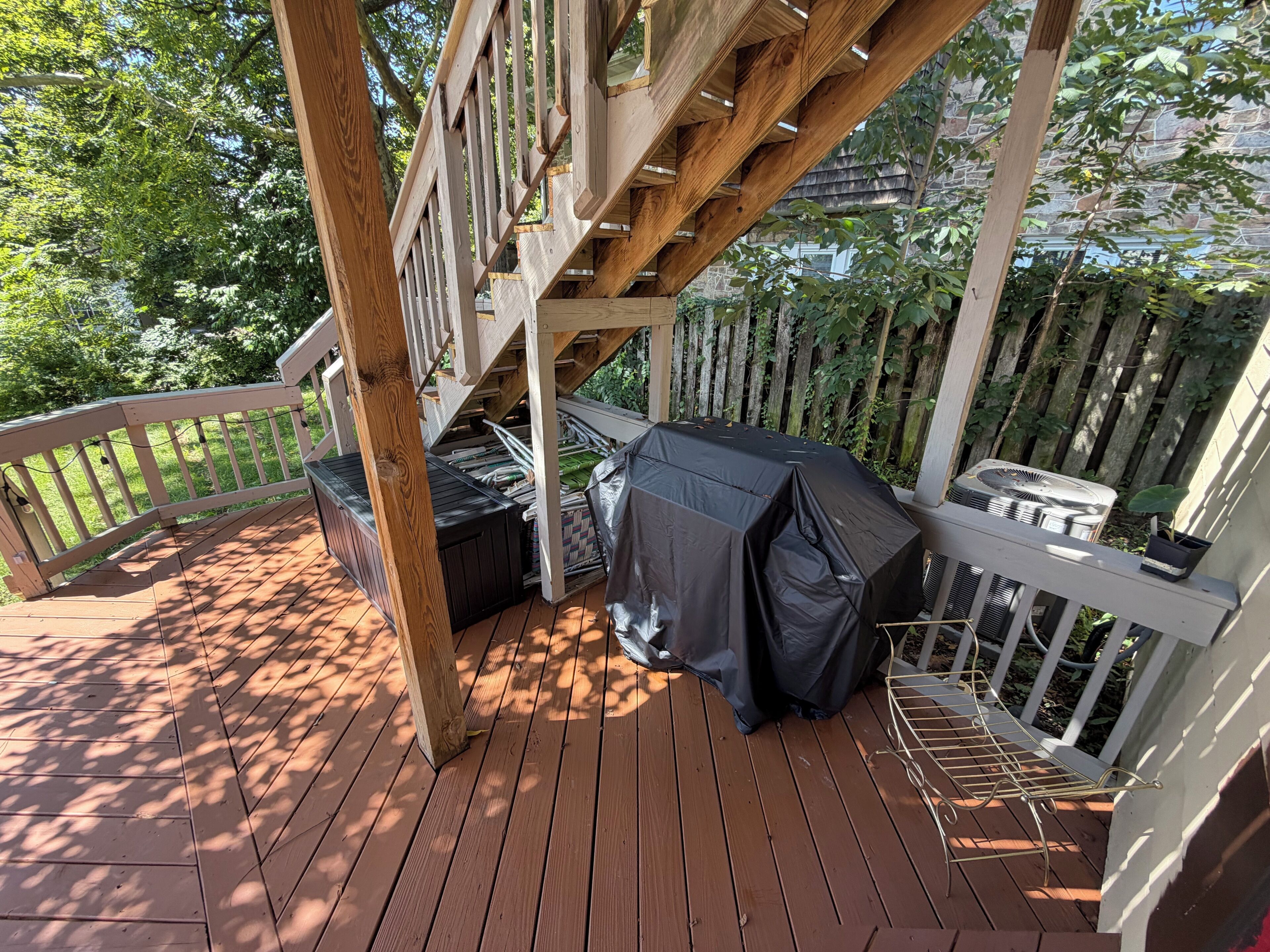 Une terrasse en bois avec un barbecue couvert et une chaise en métal.