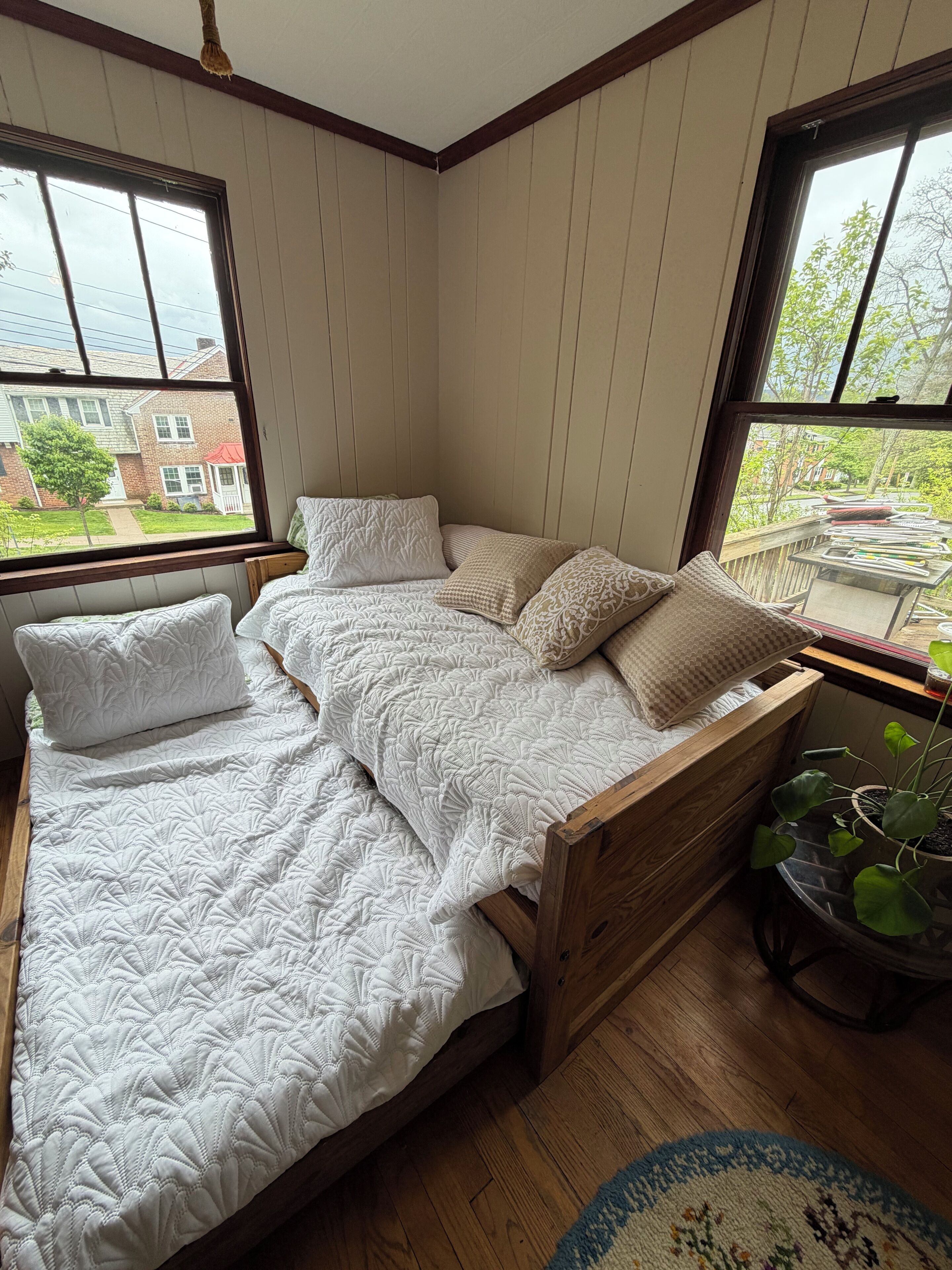 Une chambre avec un lit en bois, une fenêtre donnant sur une maison en briques et une plante en pot.