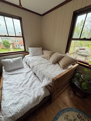 A bedroom with a wooden bed, a window with a view of a brick house, and a potted plant. - Charming 3-bedroom house in State College (State College)