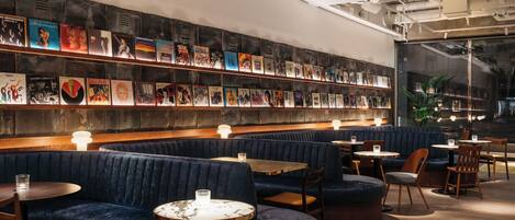A restaurant with dark blue booths, wooden tables, and a wall of bookshelves.