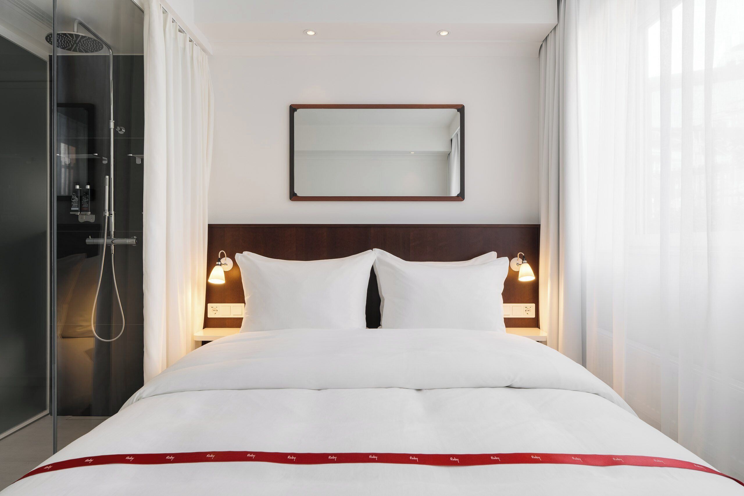 A hotel room with a bed, a shower, a mirror, and bedside lamps.