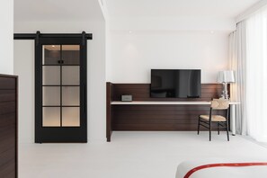 A modern hotel room with a sliding door, a flat-screen TV, a desk, and a chair.