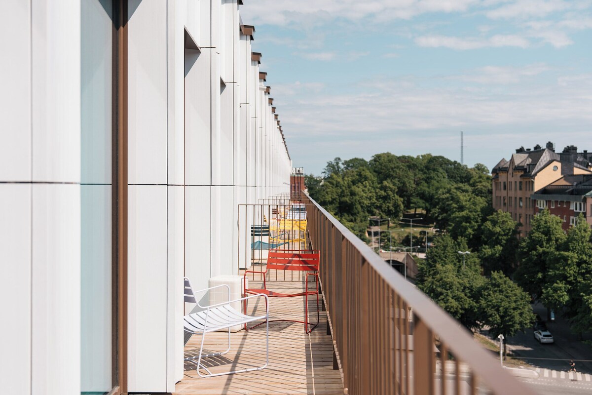 A balcony with a view of a city street, a railing, and a chair.
