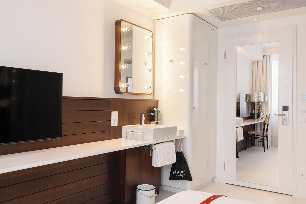 A modern bathroom with a vanity, mirror, lights, and a television.