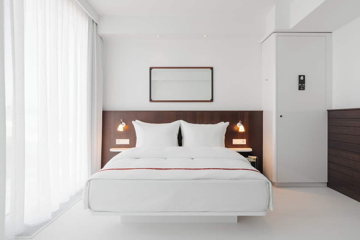 A modern hotel room with a large bed, bedside lamps, a framed mirror, and a door with a lock.