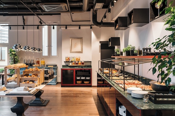 A breakfast buffet with various food items, a coffee station, and a plant in the foreground. - Ruby Frida Hotel Stockholm By IHG (Stockholm)