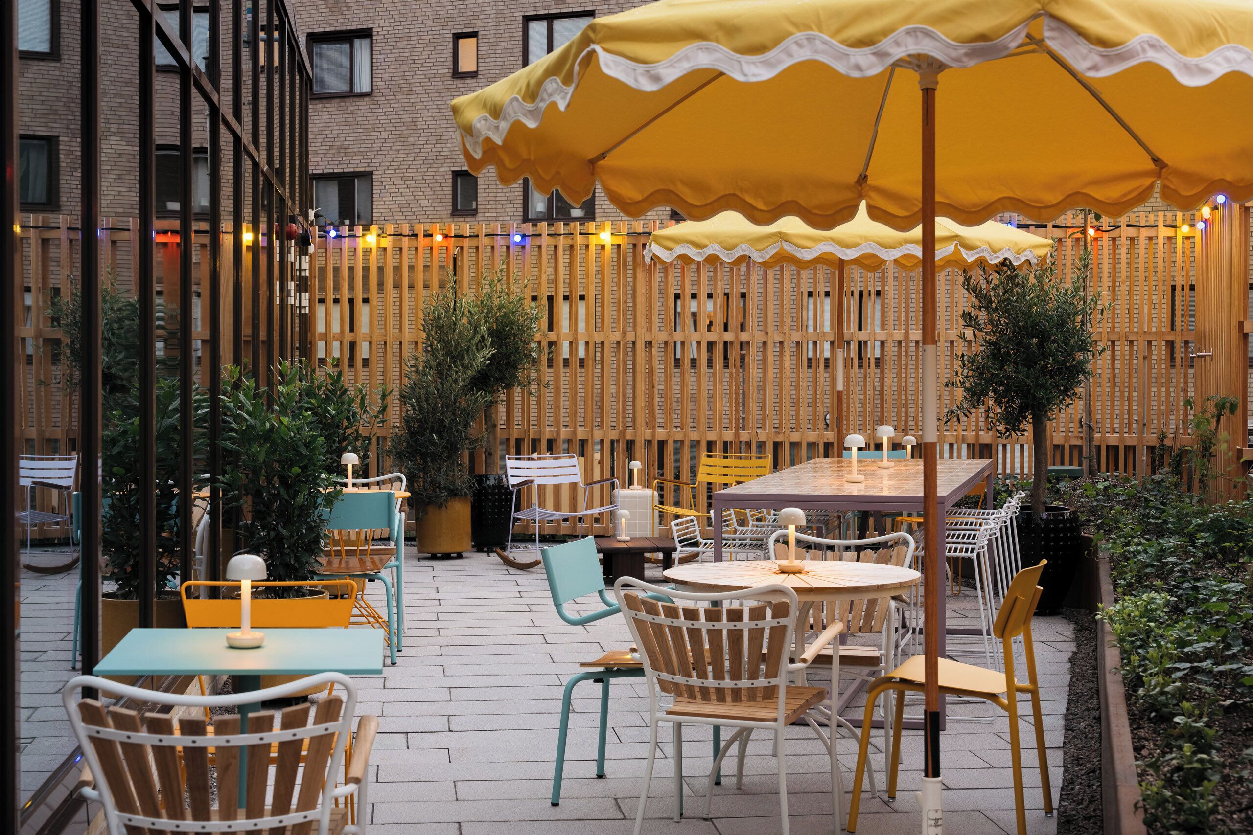An outdoor patio with tables and chairs, a wooden fence, and string lights.