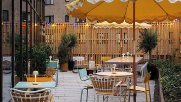 An outdoor patio with tables and chairs, a wooden fence, and string lights.