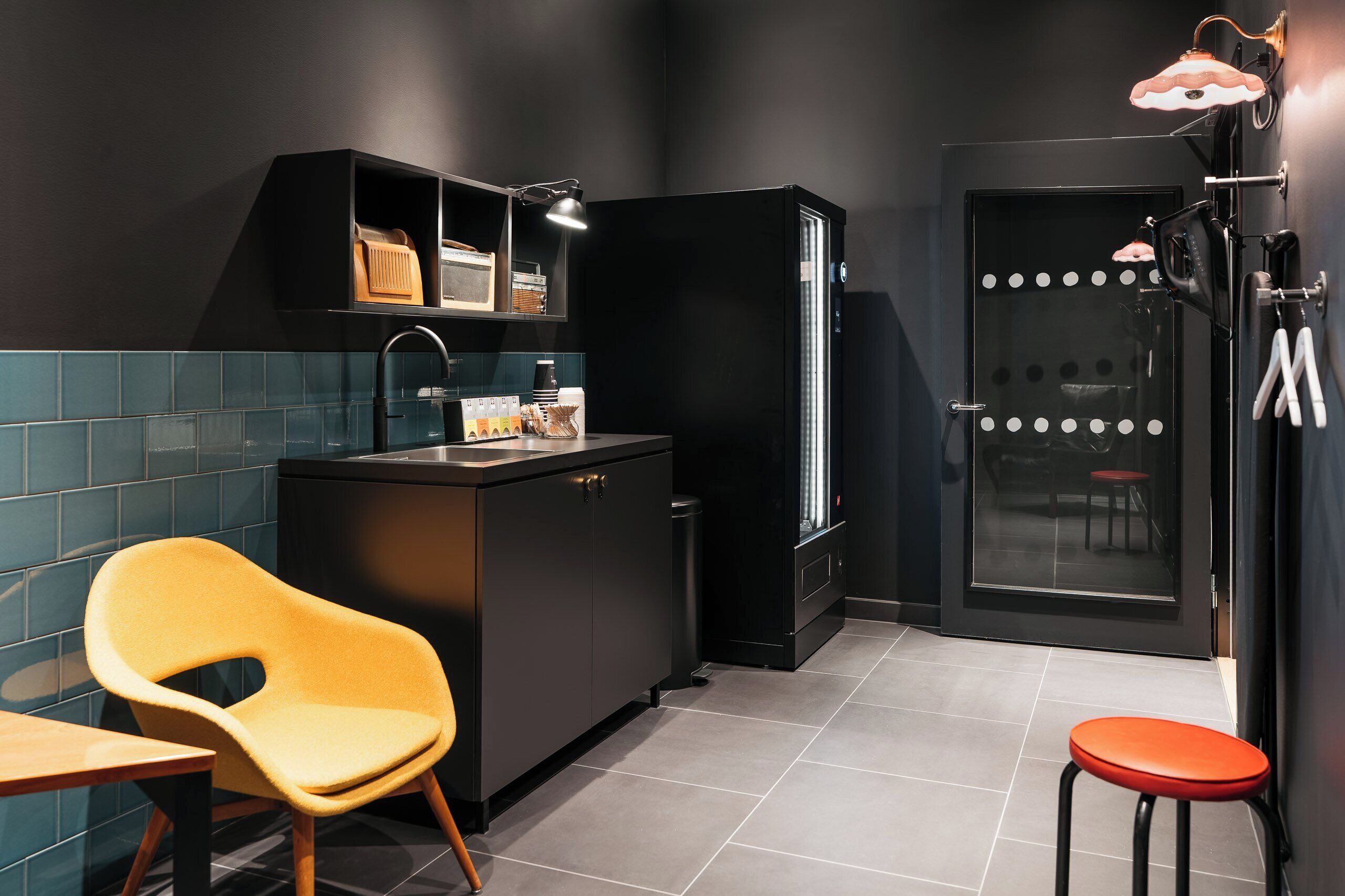 Une petite cuisine équipée d’un évier, de placards et d’un réfrigérateur. La pièce contient également une chaise et un tabouret.