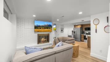 A modern living room with a fireplace, a sofa, a coffee table, and a kitchen in the background.