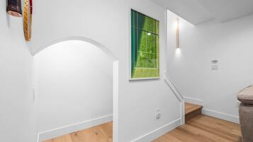A staircase with a green tennis court view, white walls, and wooden flooring.