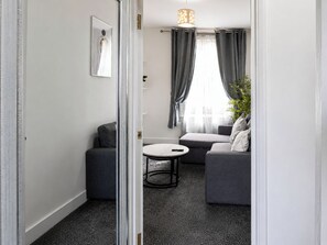 A modern living room with a sofa, a small round table, and a potted plant. - One Bedroom Luxury Apartment (London)