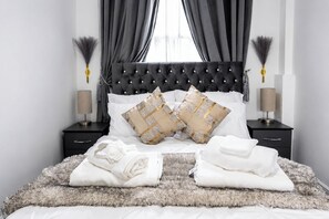 A neatly made bed with two decorative pillows, a fluffy rug, and two bedside tables with lamps. - One Bedroom Luxury Apartment (London)