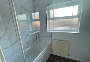 Ein Badezimmer mit einer Badewanne, einem Fenster und einer Marmorwand.