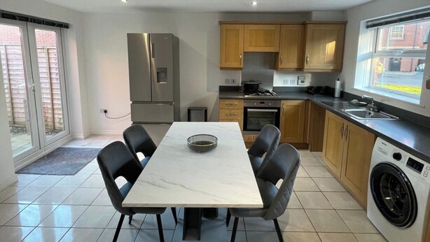 Una cocina moderna con una mesa de comedor, sillas, refrigerador, horno, lavadora y una ventana.