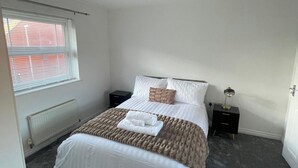Un dormitorio con cama, mesita de noche, lámpara, radiador y ventana con persianas.