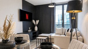 Moderni olohuone, jossa on litteänäyttöinen televisio, lasinen sohvapöytä, sohva ja lattiavalaisin.
