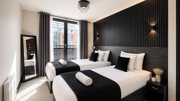 Hotellihuone, jossa on kaksi sänkyä, suuri peili, näkymä rakennuksiin ja moderni valaisin.