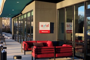 An exterior of a hotel with a red sofa, a 'Welcome' sign, and glass doors. - Avid Hotel Kingman - Medical Center Area By Ihg (Kingman)