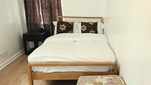 Un letto con struttura in legno, biancheria bianca e cuscini a motivi floreali.