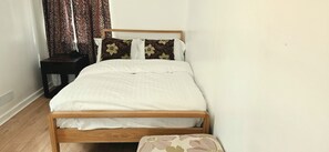 A bed with a wooden frame, white bedding, and floral-patterned pillows. - Apartment Sleeps 4 with WiFi (Clacton-on-Sea)