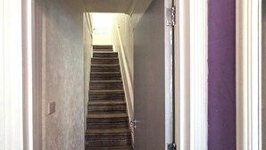 Un corridoio stretto con una scala in legno che conduce a un pianerottolo.