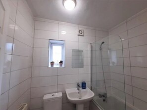Een badkamer met witte tegels, een raam met planten, een wastafel en een douche.