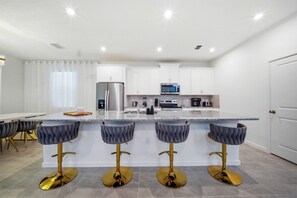 This stylish kitchen boasts a spacious island with elegant gold-accented stools, ideal for casual meals or morning coffee, while bright white cabinetry and modern appliances create an inviting atmosphere for delightful cooking. - 6BR house sleeps 13 with spa and pool table (Kissimmee)