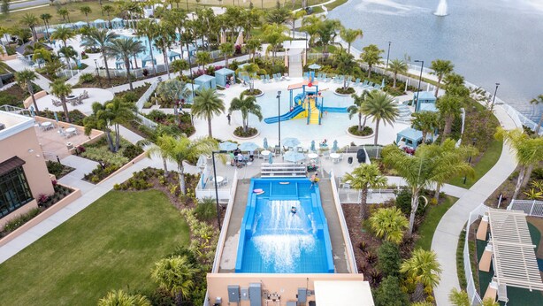 A resort pool area with a central water slide, surrounding lounge chairs, and palm trees. - 6BR house sleeps 13 with spa and pool table (Kissimmee)