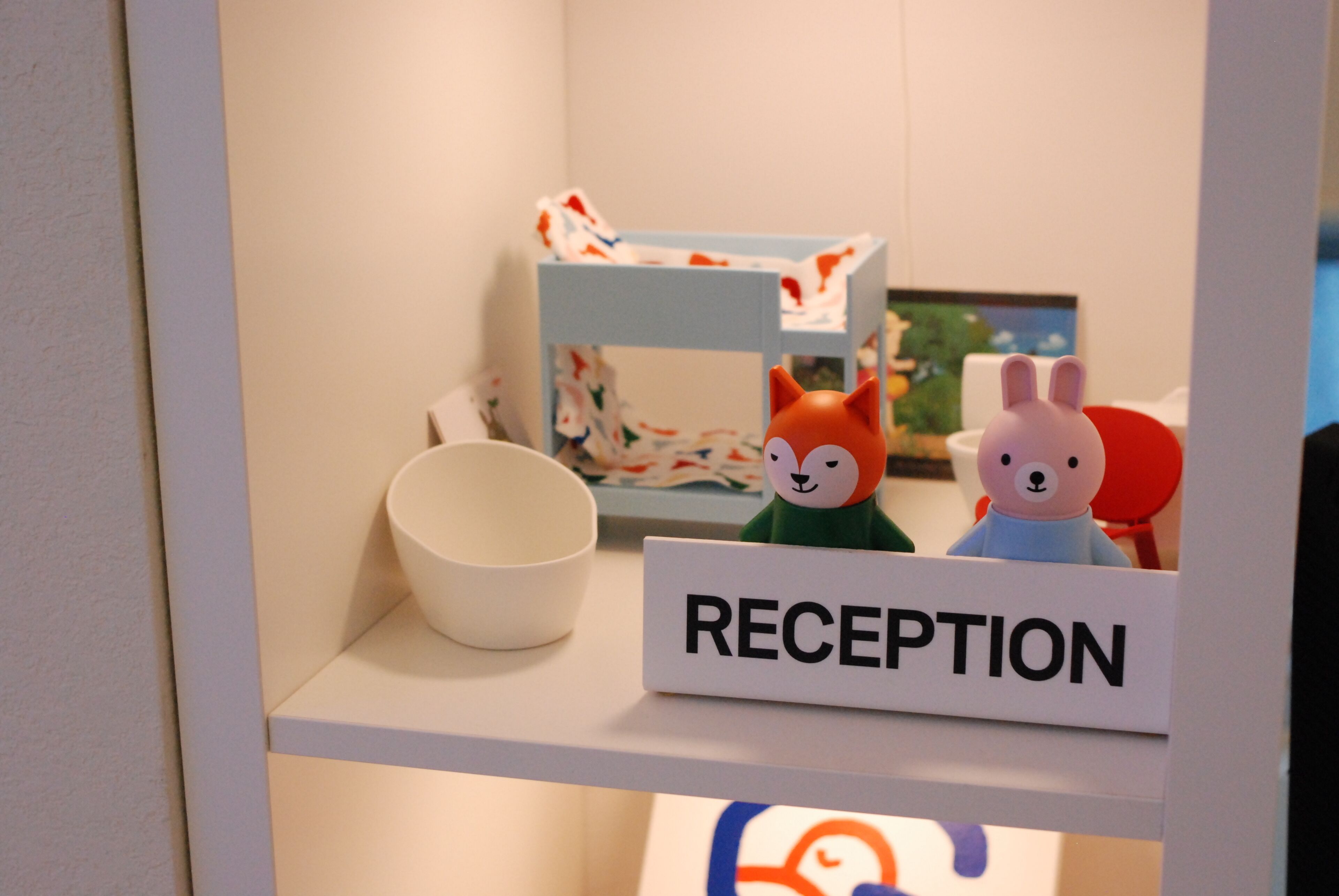 A reception area with a sign labeled 'RECEPTION,' a white bowl, and two figurines on a shelf.