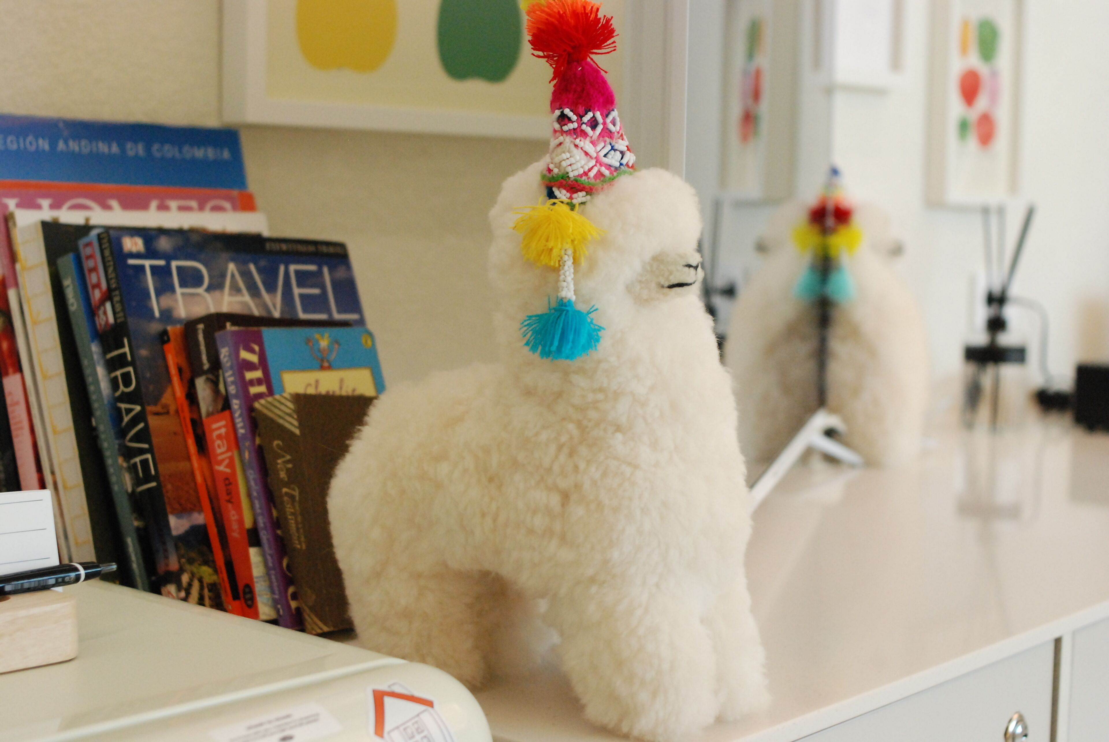A white fluffy dog with a colorful hat sitting on a counter with books.