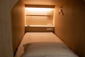 A small, narrow room with a bed, a shelf with a light, and a 'DO NOT DISTURB' sign. - Good Day Cube Seomyeon Capsule Hotel (Busan)