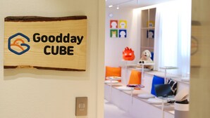 A sign with 'Goodday CUBE' logo, a modern interior with white walls, and colorful artwork.