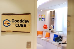 Een bord met het 'Goodday CUBE' logo, een modern interieur met witte muren en kleurrijke kunstwerken.