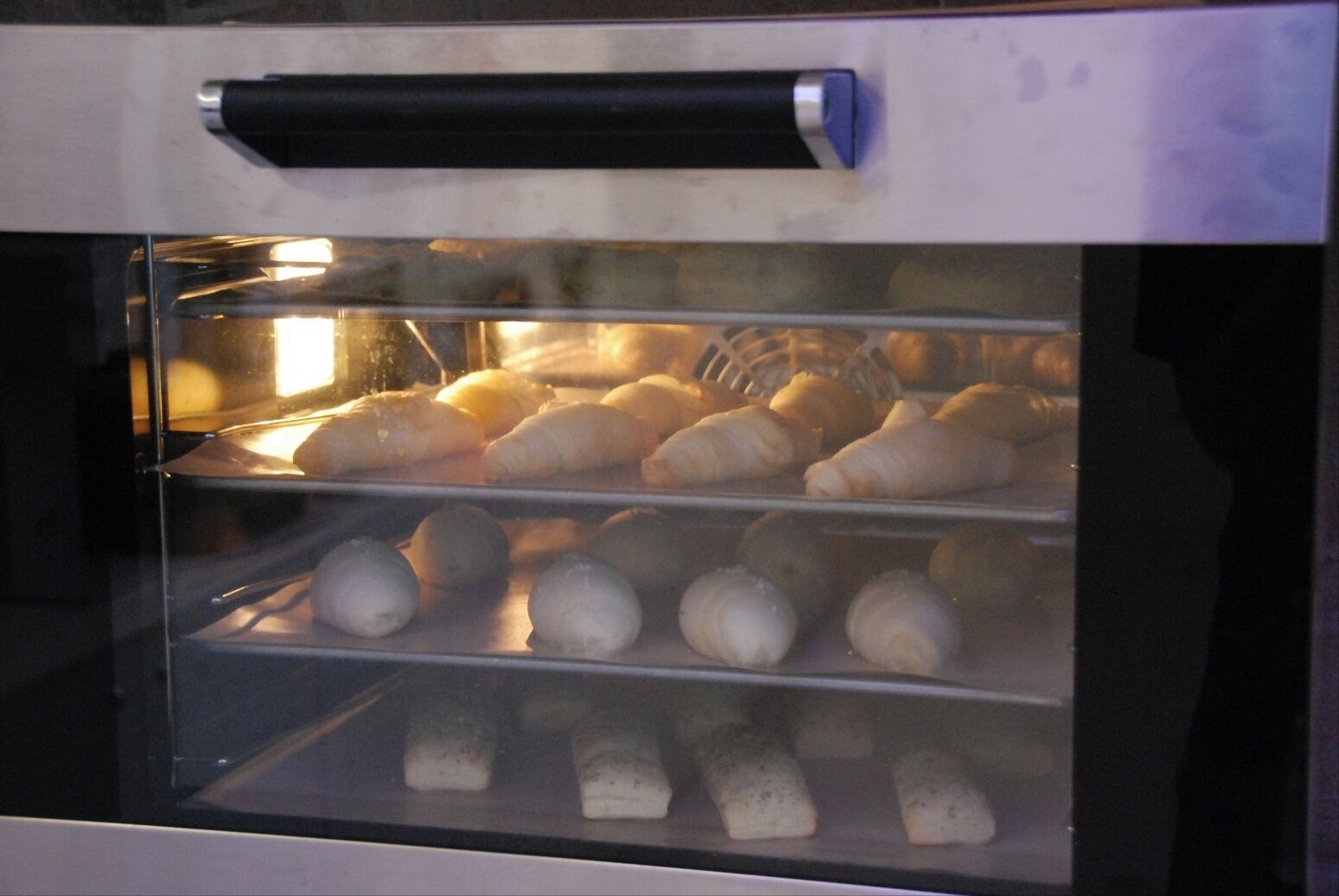 Forno com várias assadeiras cheias de produtos de panificação.
