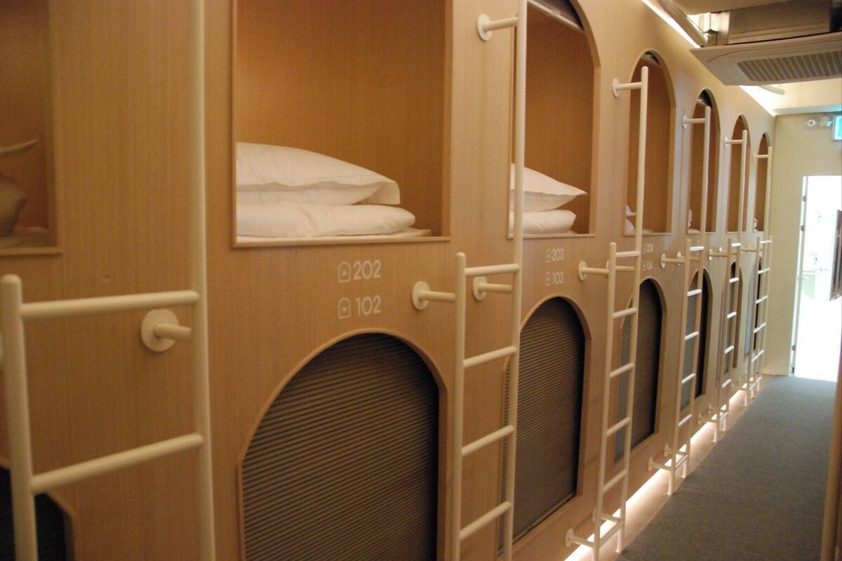 Een rij houten kamers met bogen, elk voor één persoon, met genummerde deuren en een klein raam.