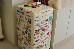 A refrigerator covered in various stickers and magnets, with a teddy bear on top.