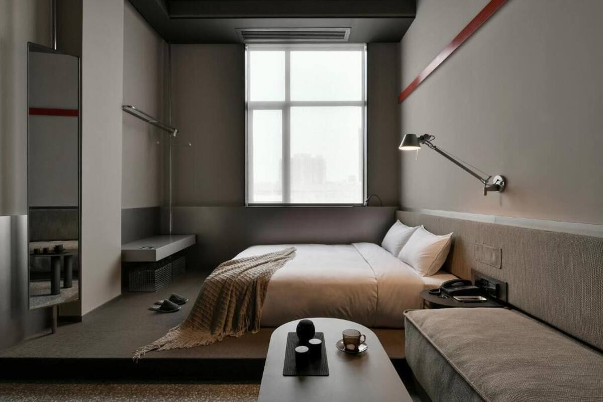 Un hotel moderno con cama, mesita de noche, lámpara y vistas a la ciudad a través de un ventanal grande.