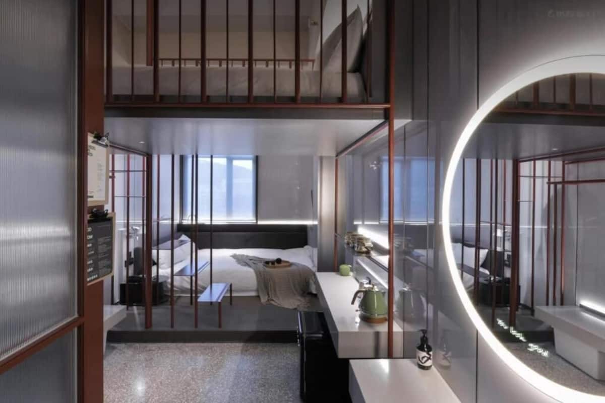Una habitación de hotel moderna con una cama litera, un espejo grande, una mesita de noche y vistas a la ciudad.