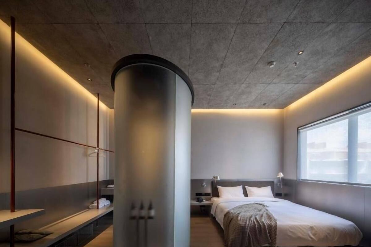Un dormitorio moderno con un objeto cilíndrico grande, una cama, una mesita de noche y un ventanal.